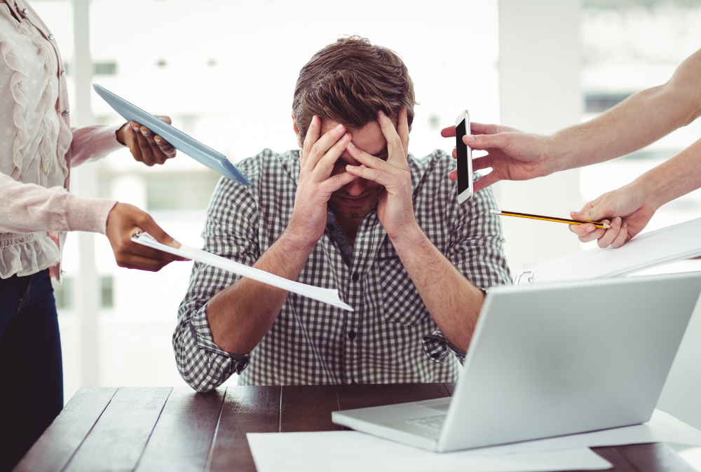 man experiencing chronic stress in front of a laptop with his hands over his eyes